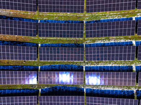 Rows of solar panels cover a green field under bright sunlight. The panels are neatly aligned and...