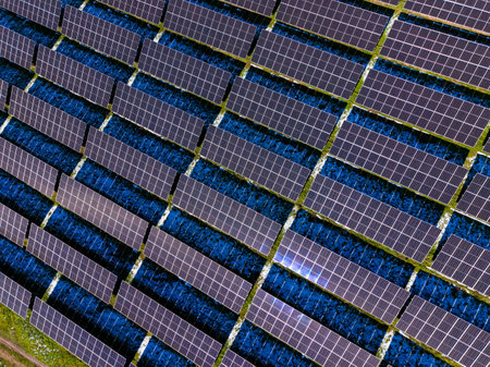 Rows of solar panels are installed on the ground in a large field. The panels capture sunlight to...