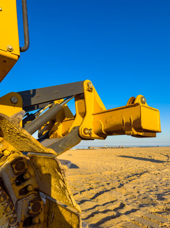 A yellow piece of construction equipment sits on the sand at the beach. The bright blue sky fills the background and the sun shines on the scene.の写真素材