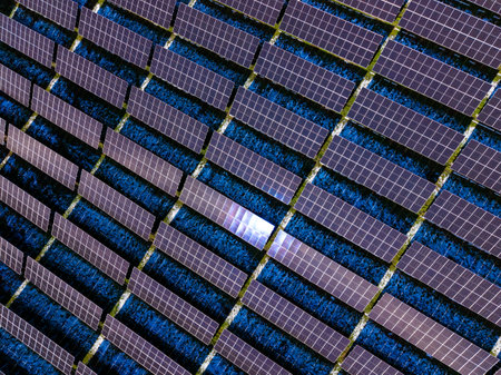 Solar panels are arranged in rows across an open land area. Blue sky and bright sunlight indicate...