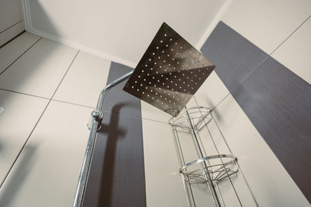 Water comes out of a large showerhead in a bathroom that has vertical striped walls. A metal shower...
