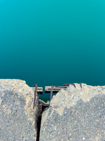 A cracked concrete pier is shown with metal anchors exposed. The pier is above clear turquoise water under bright sunlight. The scene captures the contrast between the pier and the water.の写真素材