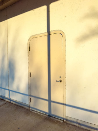 A door situated on the side of a building shows a shadow from a railing in the sunlight. The...