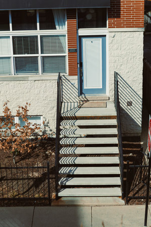 Stairs provide access to a door at a building during bright daylight. Shadows from the railing...