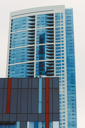 Tall glass building reflects the sky and has many balconies in a city with clouds above and nearby...