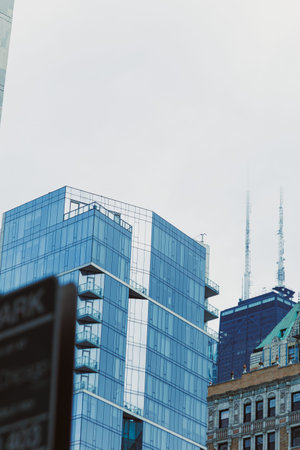 Two buildings are seen side by side in a city. One is made of glass and reflects the sky. The other...