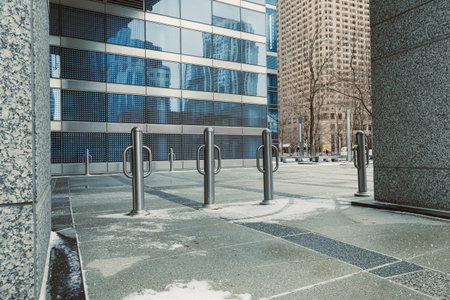 Snow is visible on the ground in a city plaza featuring metal poles and glass buildings reflecting...