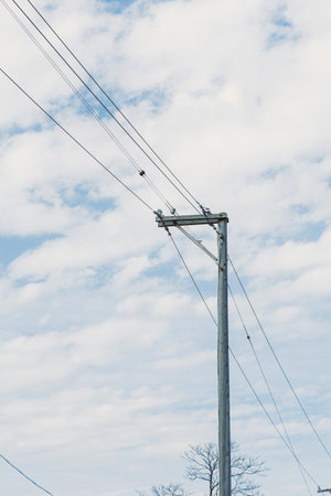 A utility pole is seen in an open area with power lines stretching against a backdrop of clouds. The...