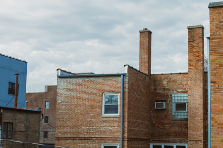 Brick buildings are lined up in an urban area. The sky is cloudy, and utility connections are...