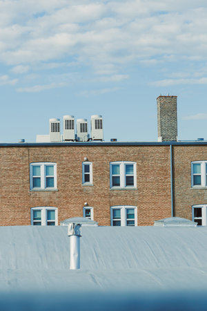 A view of building rooftops in a city. Two buildings show windows and air conditioning units. A...