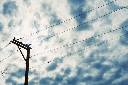 Power lines stand tall against a backdrop of clouds that block sunlight during the day. The setting...