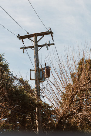 Two workers check the power line from a utility pole in a neighborhood setting. The sky is clear,...