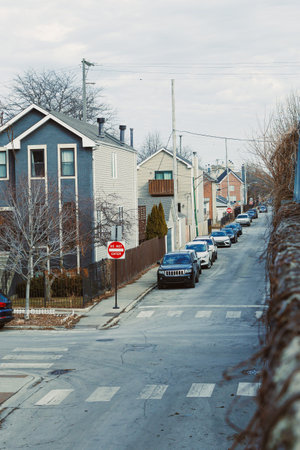 Cars are parked along a street with houses on both sides. The sky is cloudy and it is daytime. The street has marked crosswalks and road signs.の写真素材