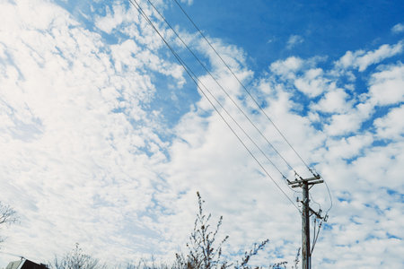 Power lines run alongside bushes as clouds fill the sky during midday. The blue sky shows a mix of...