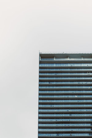 A tall office building with a glass exterior is shown against an overcast sky in a city setting...