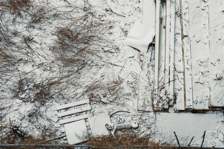 White snow blankets old wooden planks and debris on the ground near a construction site during a...