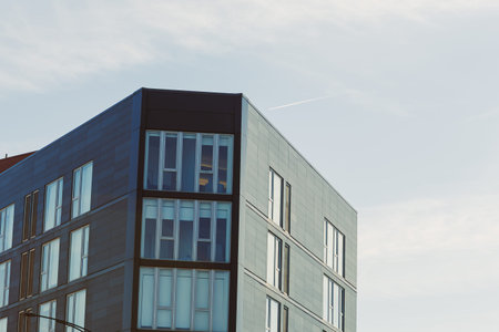 A tall building with large windows sits at the edge of an urban area. The sky is clear, and a small...