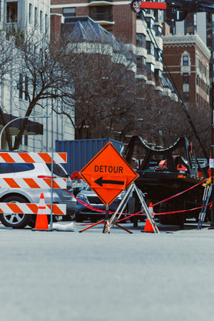 Traffic signs are present in a construction area blocking part of the street. Cars move around the...