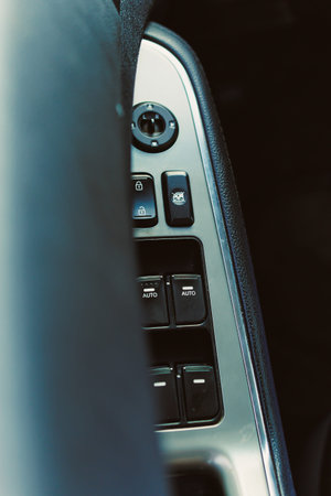 Close view of a car door panel showing buttons for windows and locks clearly laid out. The sun...