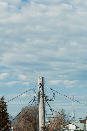 A wooden utility pole rises in a suburban neighborhood with wires attached running down. Clouds fill...