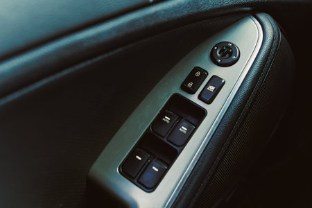 A close view of a car door control panel showing various buttons for windows and locks. The photo...