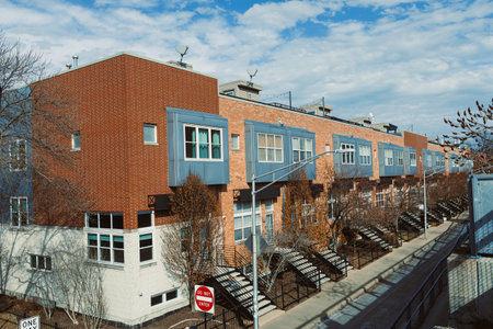 Townhouses are visible along a sidewalk with trees in view. The sky is partly cloudy and it looks...