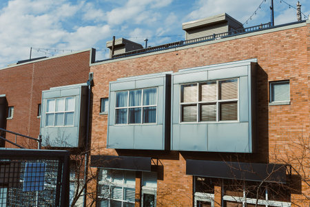 In an urban setting, a building shows large windows and metal panels on its exterior. Clear skies...
