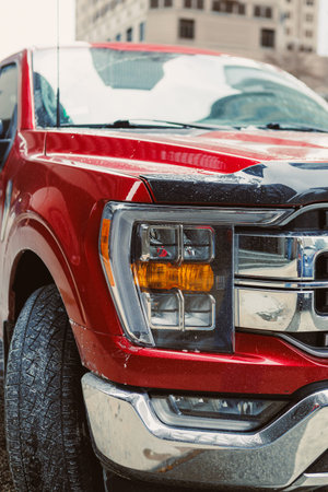 A red truck is parked on a city street. The truck has dirt on its surface. Buildings are seen in the...