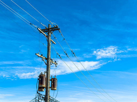 Power lines run along a wooden pole with transformers hanging below. The sky is blue with some white...