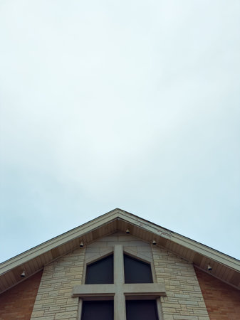 A building features a large cross on its facade, with cloudy skies above. The structure is located...
