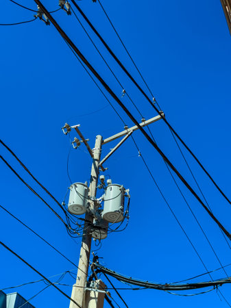 A utility pole stands tall with transformers attached. Many cables stretch out in different...