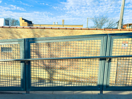 A group of people walk along a path next to buildings with brick walls under a bright blue sky. The...