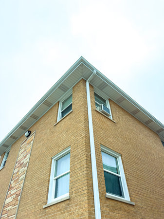 A brick building has a close-up view of its corner, showing windows and an air conditioning unit....