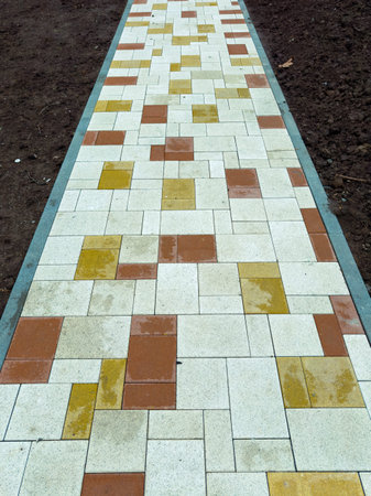 Workers have just finished laying out a pathway in a garden using square paving stones in different...