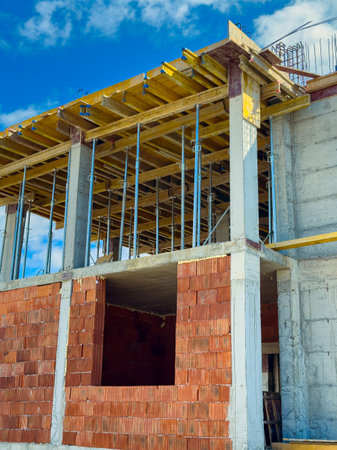 Workers are building a structure with brick walls and scaffolding in a construction area. The scene...