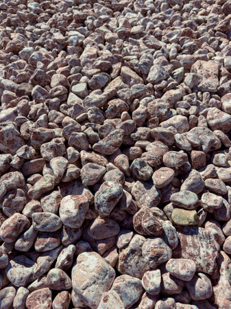 A vast area shows various sizes of smooth rocks spread across the ground. Sunlight falls on the...