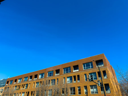 A clear blue sky stretches over a brick building in an urban area during the daytime. Sunlight...