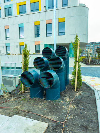 Several ventilation pipes are arranged together outside a modern building. Small trees are planted nearby on the construction site. The area looks organized and ready for finishing touches.の写真素材