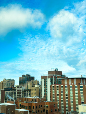 Tall buildings stand against a blue sky with clouds in an urban setting during the day. The scene...