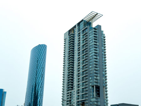 Two tall buildings rise into the sky in a city setting with a gray sky, giving a sense of modern...