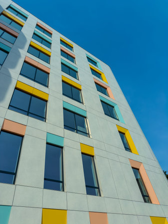 A new building stands with large windows framed in different colors. The sky above is blue. The...