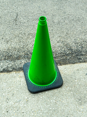 A green traffic cone is placed on the asphalt surface beside a road. The area is well lit and shows signs of wear.の写真素材