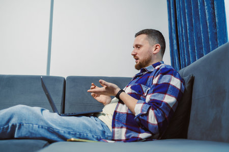 A man is sitting comfortably on a couch in a living room. He is talking and gesturing with his hands...