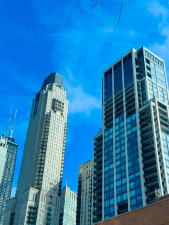In a busy city, tall buildings rise against a clear blue sky. People stroll on the street below,...