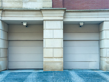 Two closed garage doors sit side by side against a brick wall. Security cameras are mounted above...