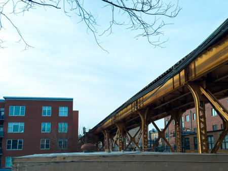 The elevated train track stretches over red brick buildings in a city. The scene shows a clear sky,...
