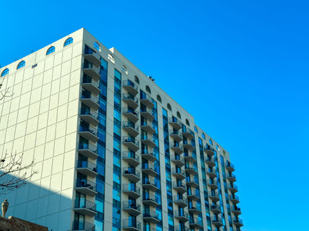 A building with many floors stands against a bright blue sky. The structure has balconies and...