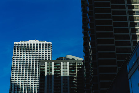 Tall buildings tower under a clear blue sky with some shadows created by their structure. The scene...