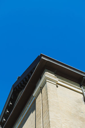 The view shows the corner of a large building under a bright blue sky. The sunlight highlights the...