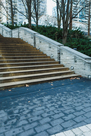 Stairs built from stone lead up to a green area filled with trees and bushes next to tall buildings...